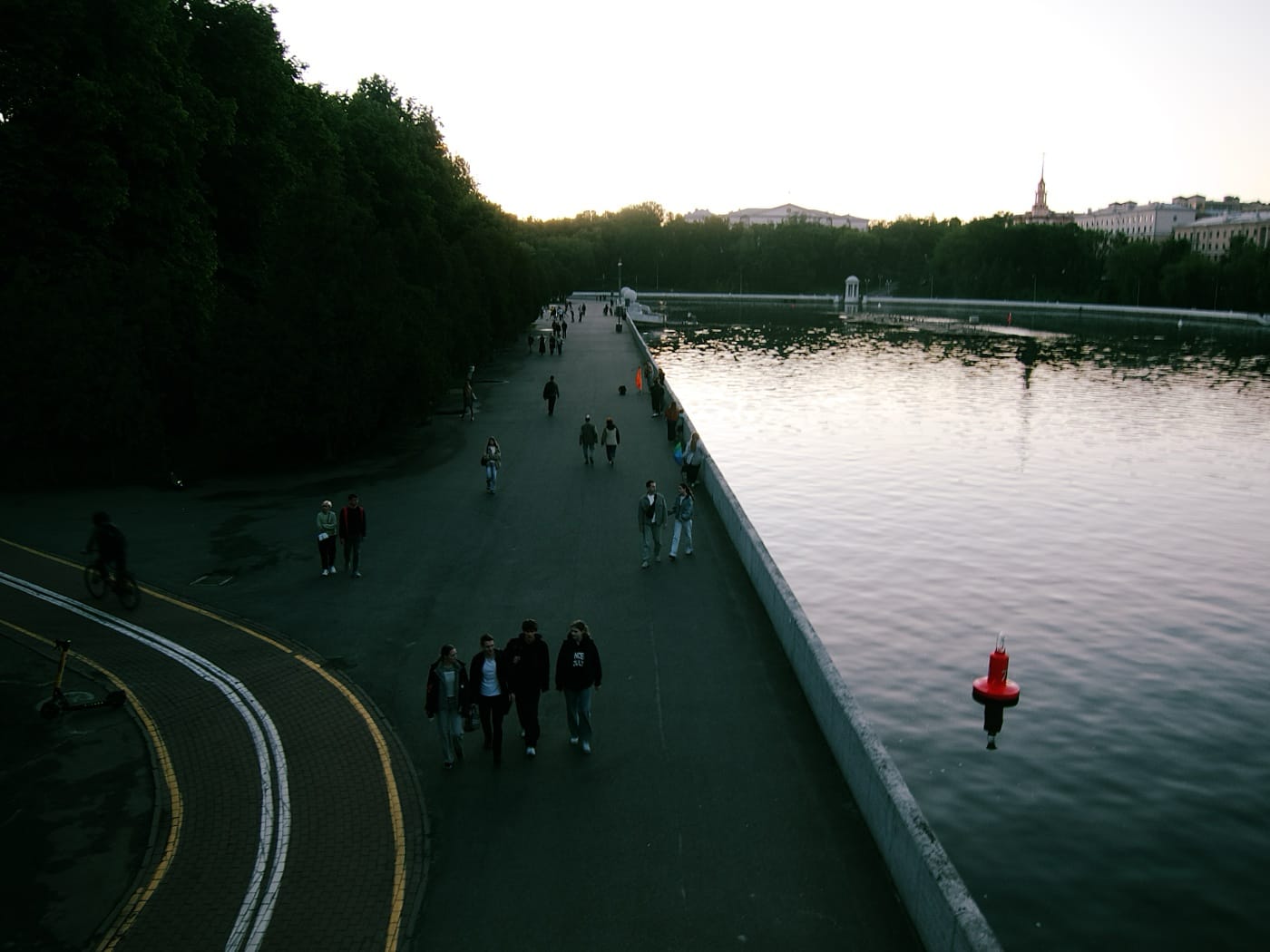 Вид с моста на вечернюю набережную Свислочи на закате: гуляют люди.