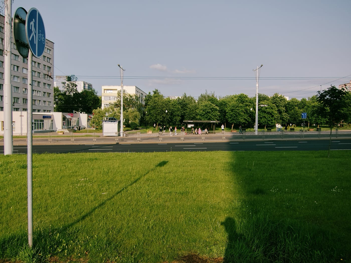Панорама города: дорога, люди стоят на остановке.