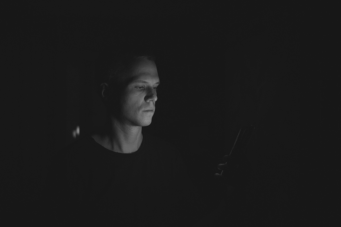 Антон Малявский в темноте смотрит на телефон, освещая лицо мягким светом.