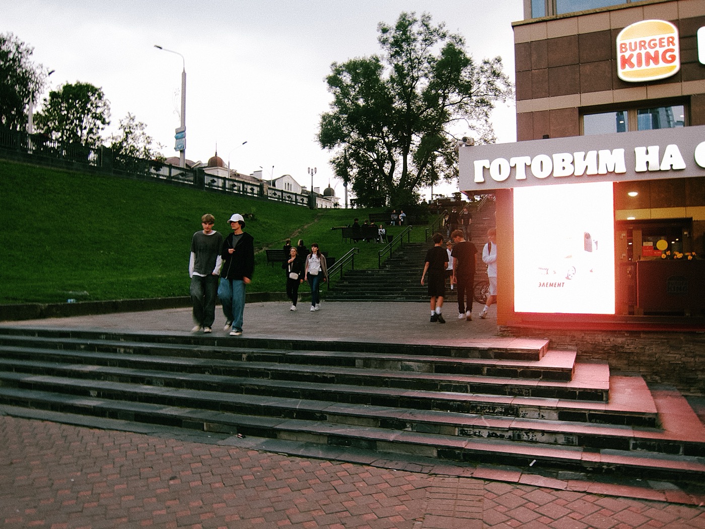 Люди гуляют по ступенькам, рядом вывеска Burger King с текстом «Готовим на гриле».