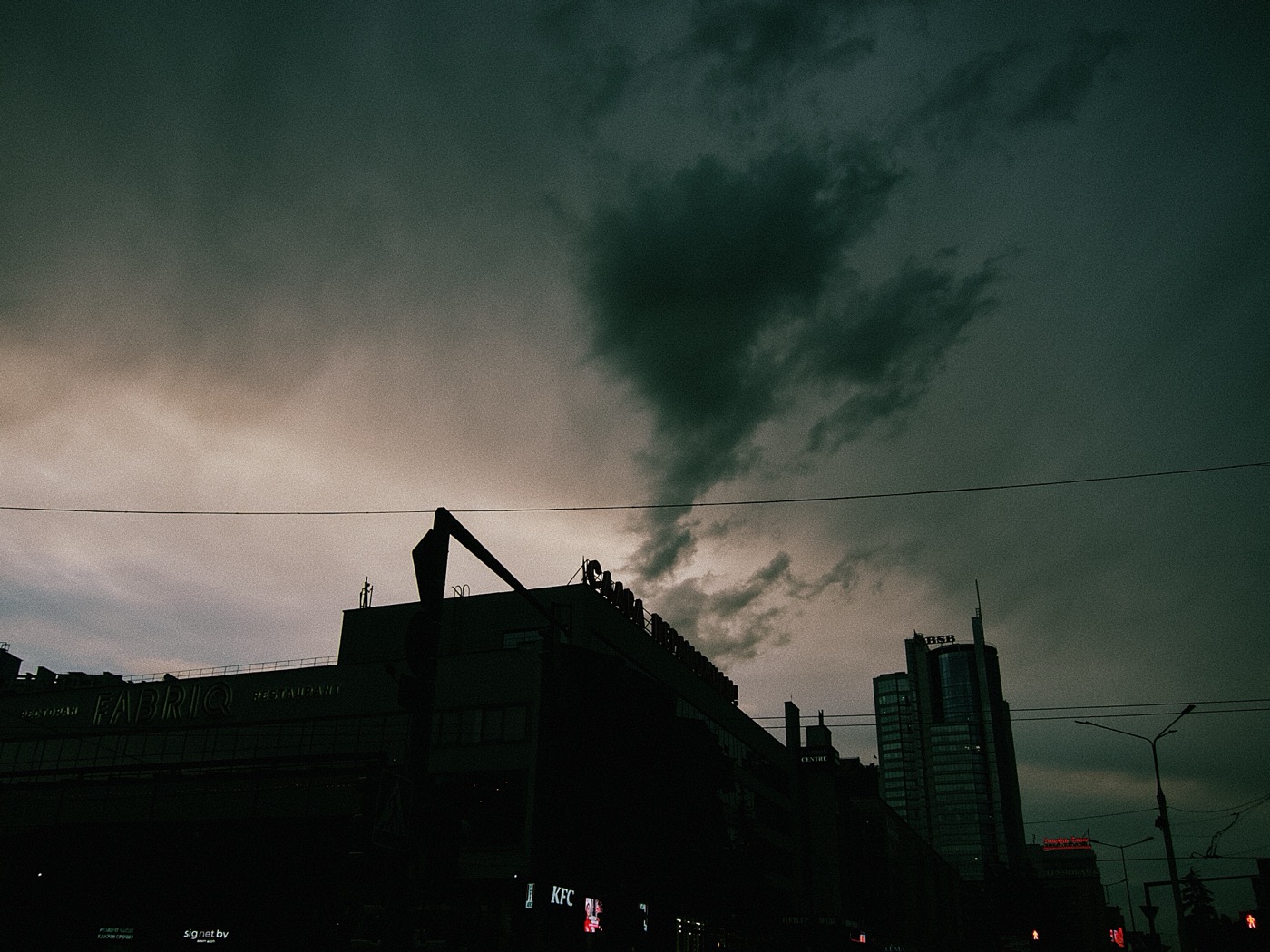 Темное небо с облаками над городскими зданиями, на горизонте видны силуэты высоток.