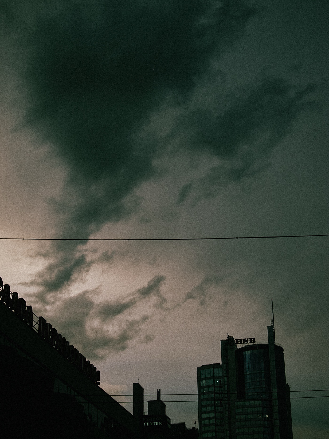 Темное небо с облаками над городскими зданиями, на одном из них виден логотип «ВТБ».