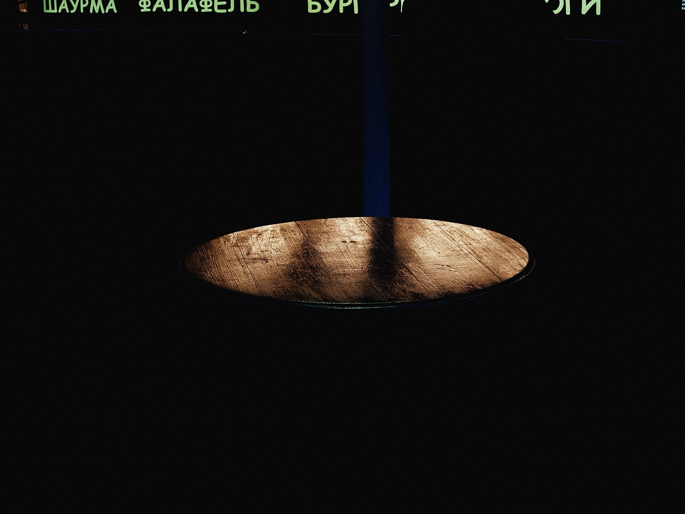 Круглый деревянный стол с ярким светом на поверхности, окружённый темнотой.