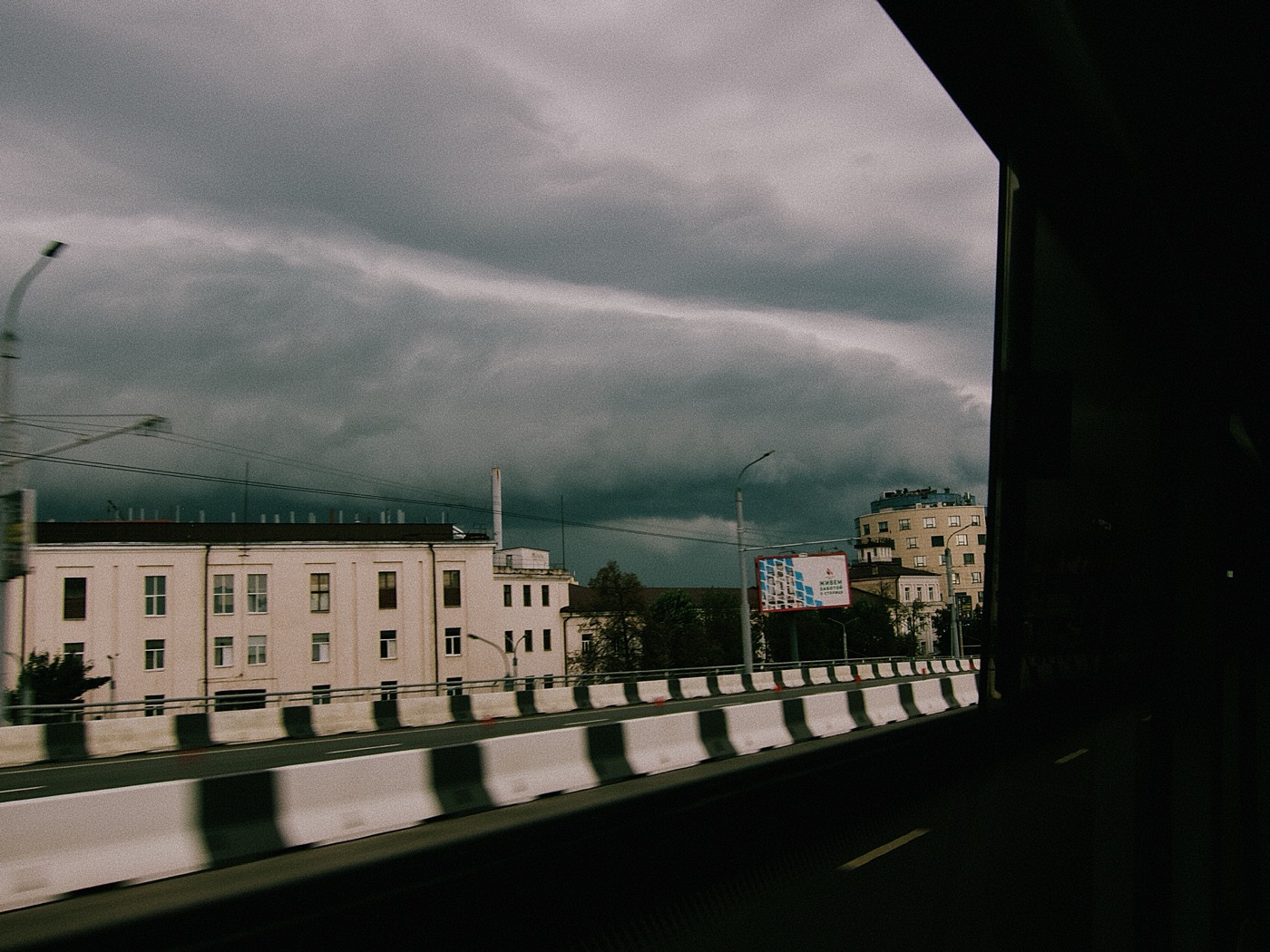 Темное небо над городом, вид из окна автобуса на дорогу и здания.