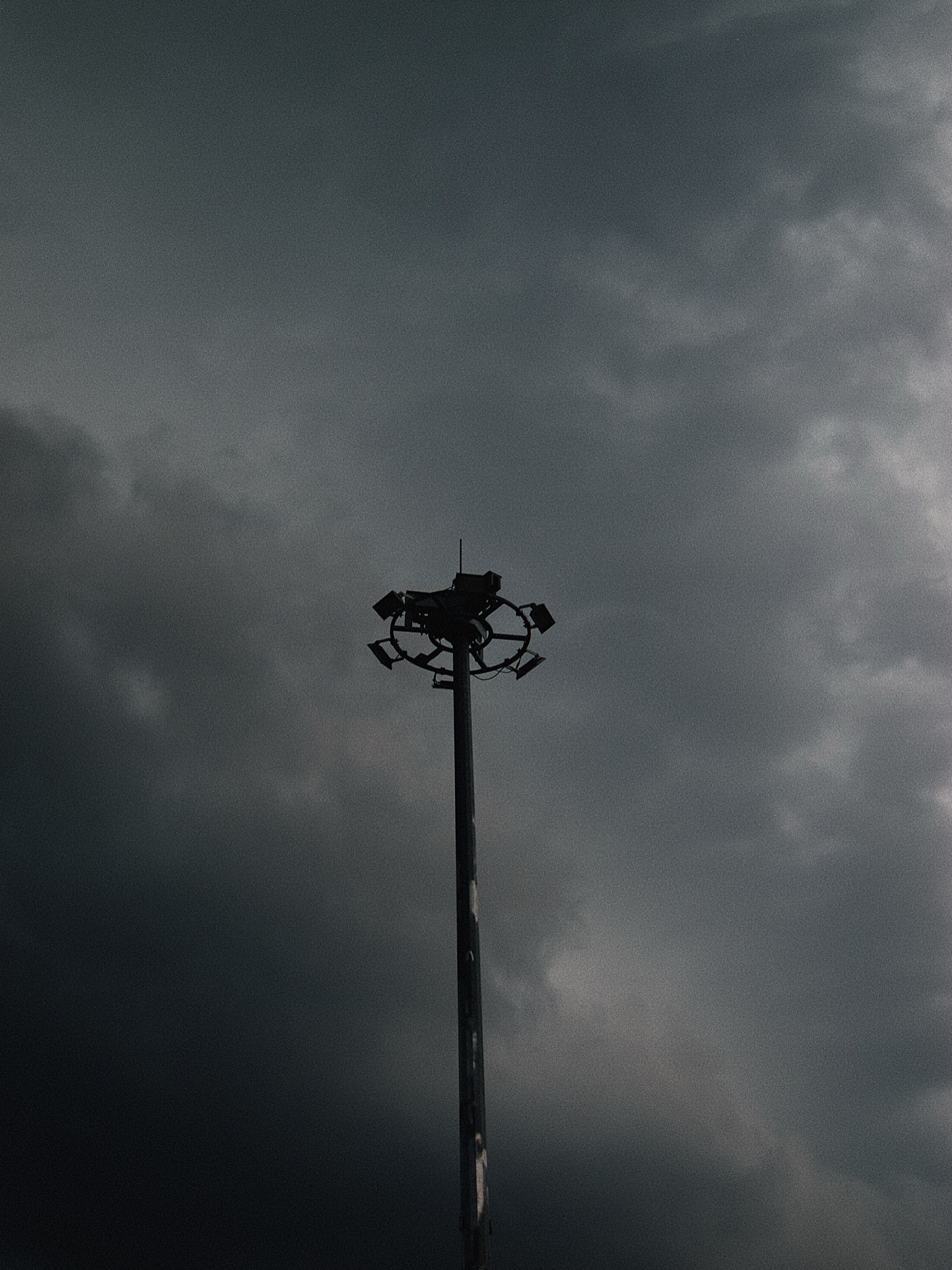 Темный облачный небосвод с одинокой мачтой, на которой установлены прожекторы.