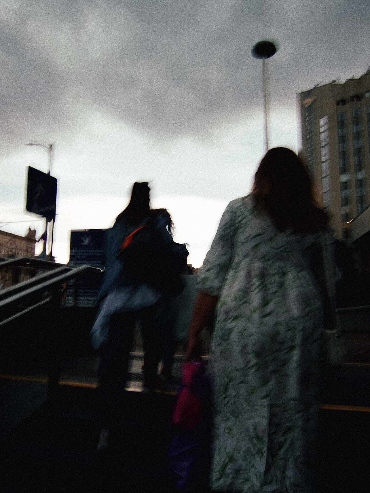 Группа людей поднимается по лестнице в условиях пасмурной погоды. На фоне видны здания и уличные фонари.