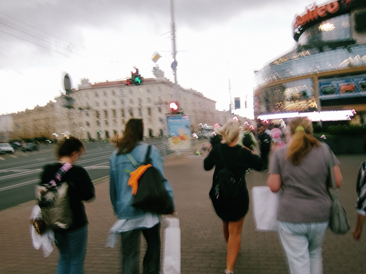 Группа людей спешит по улице, на заднем плане виден светофор и здания. Небо затянуто облаками.