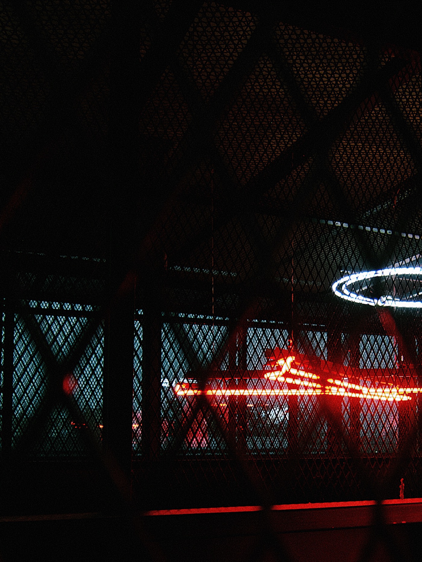 Неоновая вывеска за решеткой, красный и синий свет создают атмосферу ночного города.