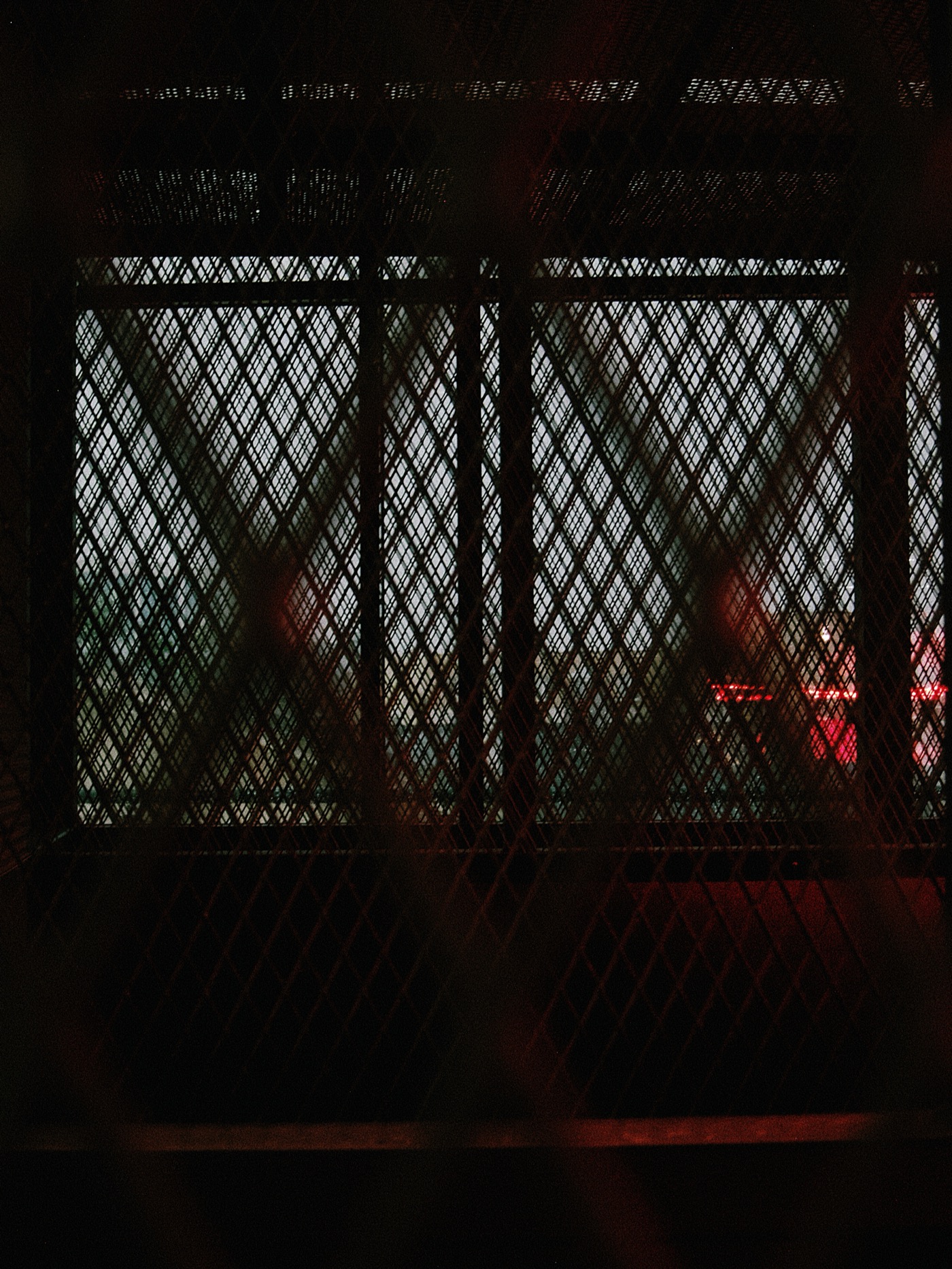 Сетка с ромбовидным узором, за которой виднеется свет и размытые силуэты.