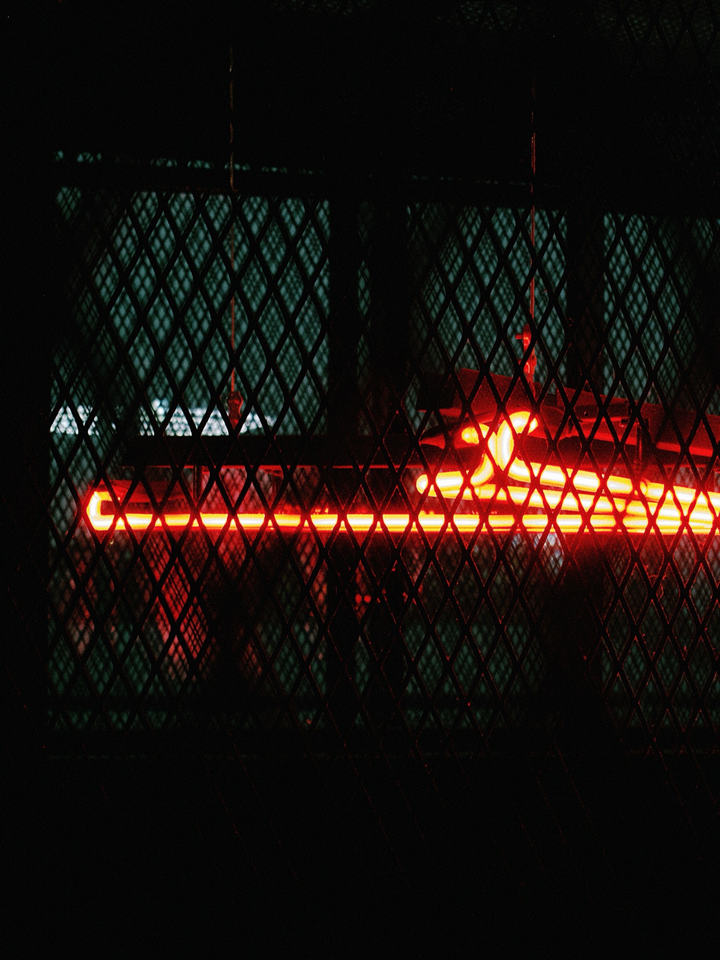 Неоновая красная вывеска на фоне сетки, создающая атмосферу загадочности.