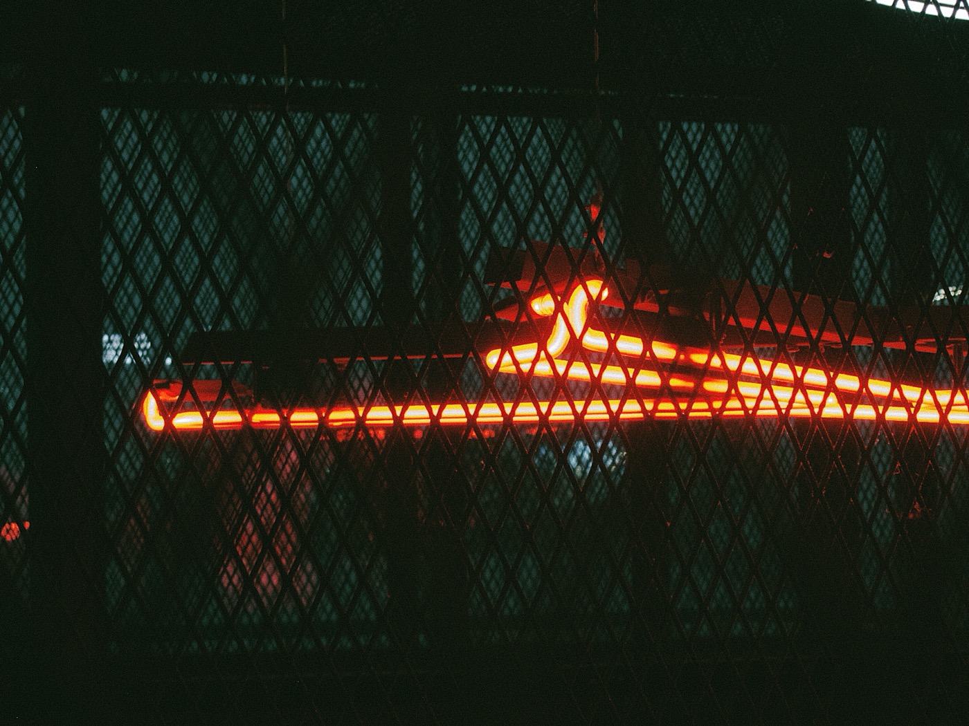 Неоновая лампа красного цвета, освещающая пространство через металлическую решетку.