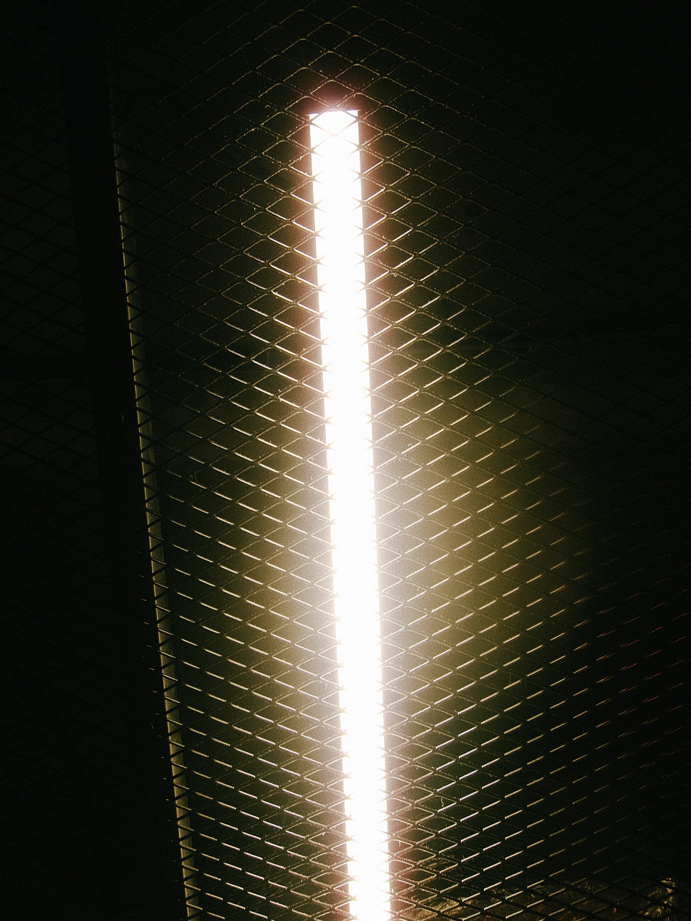 Яркая световая линия на фоне металлической сетки.