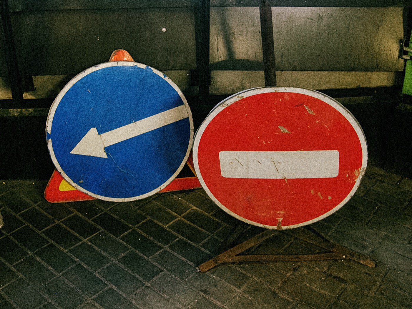 Два дорожных знака: синий с стрелкой влево и красный с белой полосой. Знаки стоят на кирпичной поверхности.