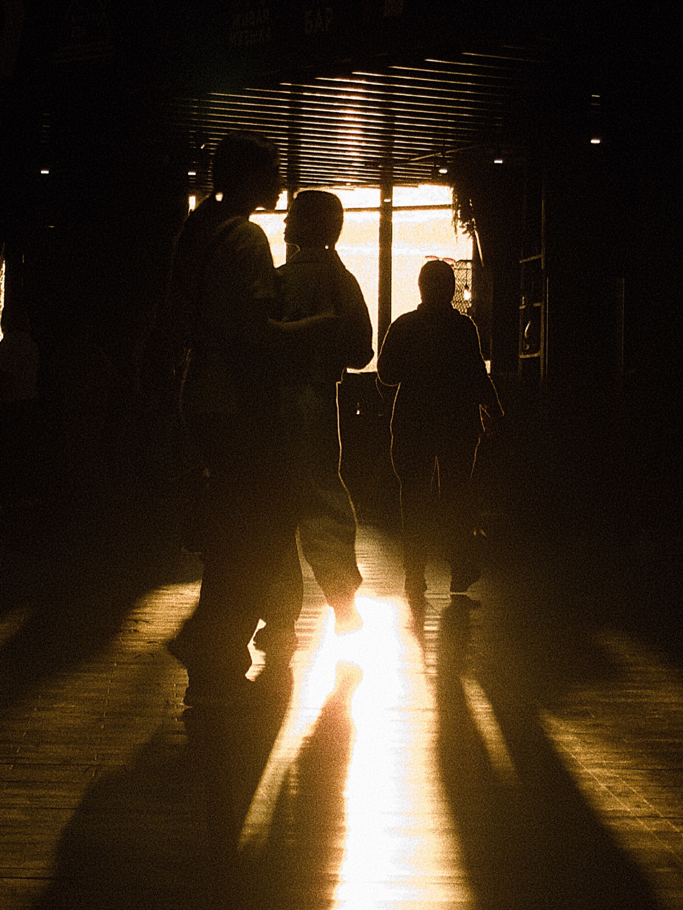 Силуэты людей на фоне яркого света, пробивающегося через окна. Длинные тени на полу.