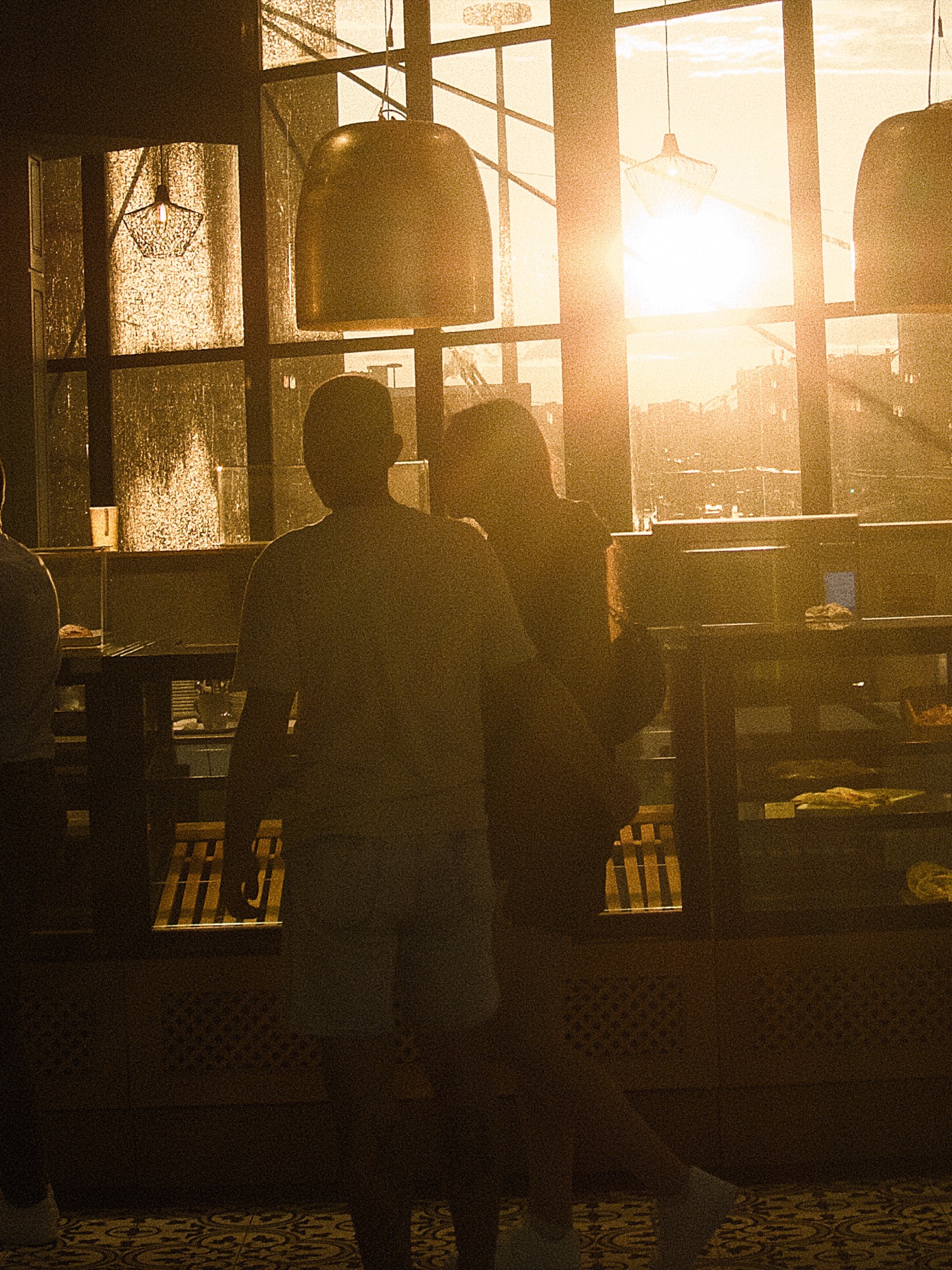 Силуэты людей на фоне заката в кафе, солнечные лучи проникают через окна.