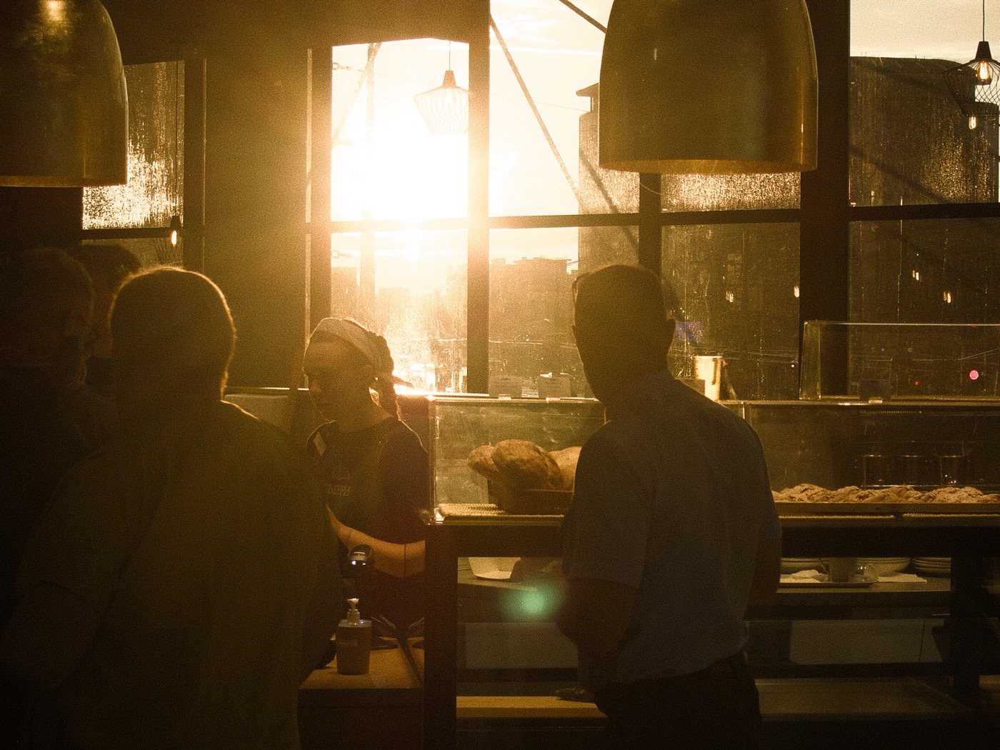 Силуэты людей в кафе на фоне заката, свет проникает через окна.