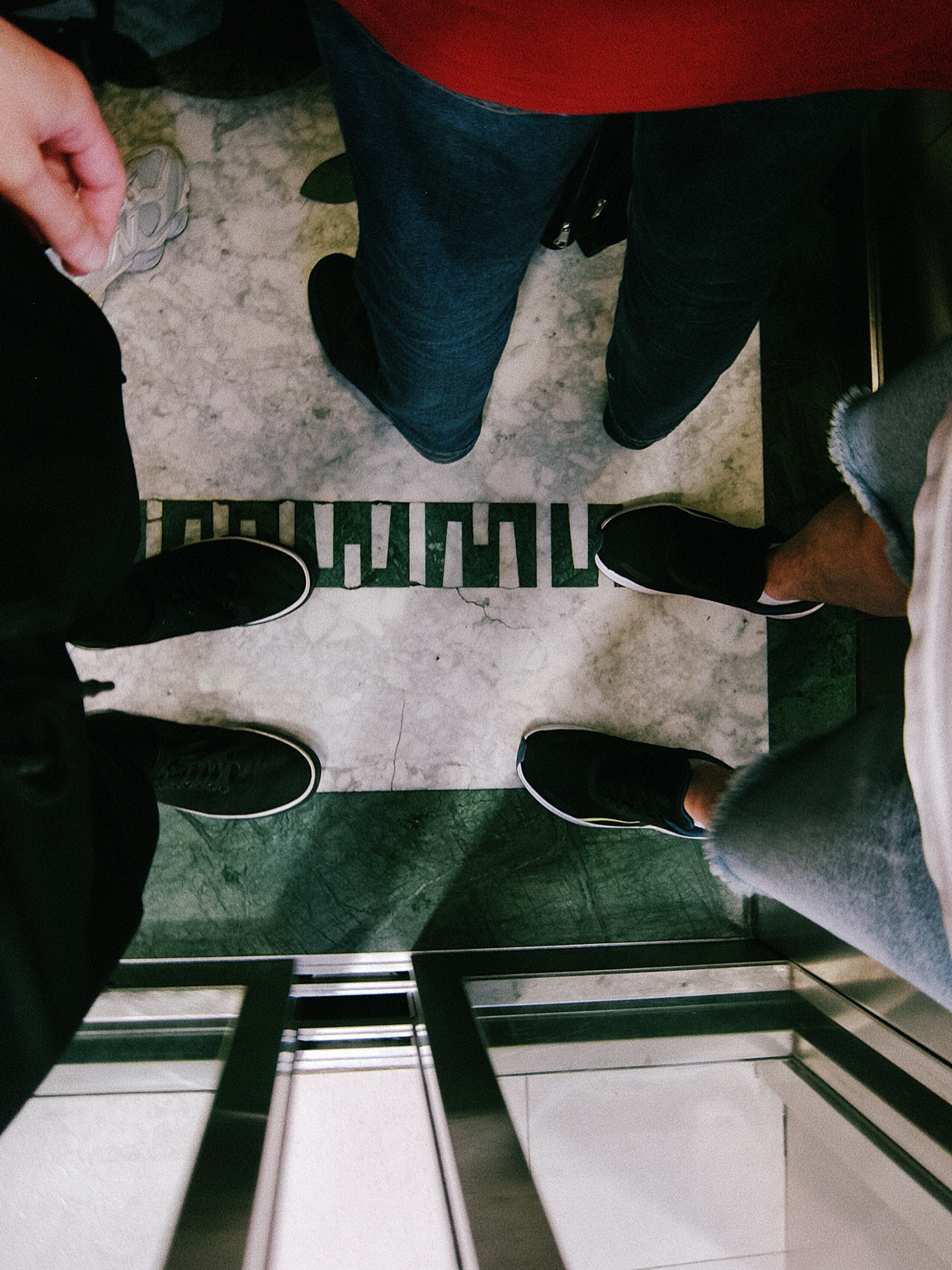Ноги людей в лифте на мраморном полу с белыми полосками.