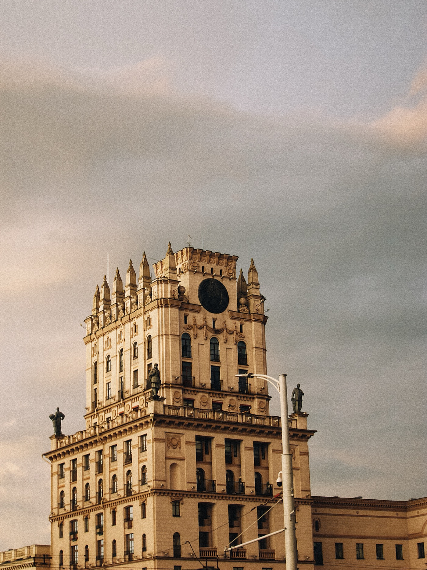 Башня с часами и статуями на крыше, облачное небо на фоне.