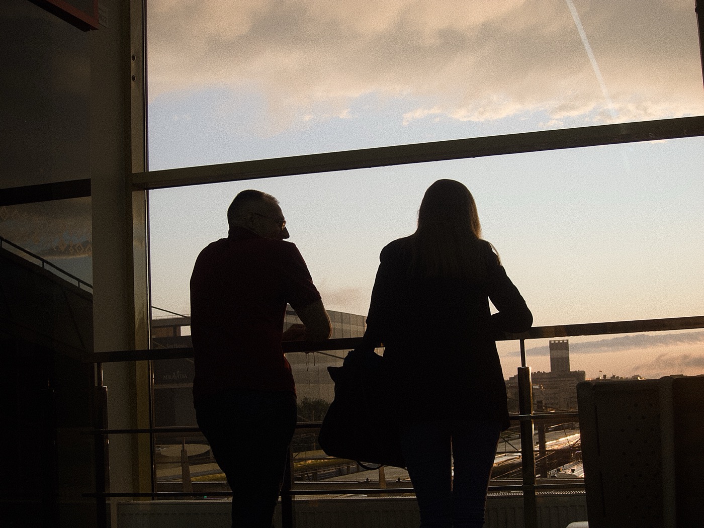 Силуэты двух человек, смотрящих в окно на закат и городские пейзажи.