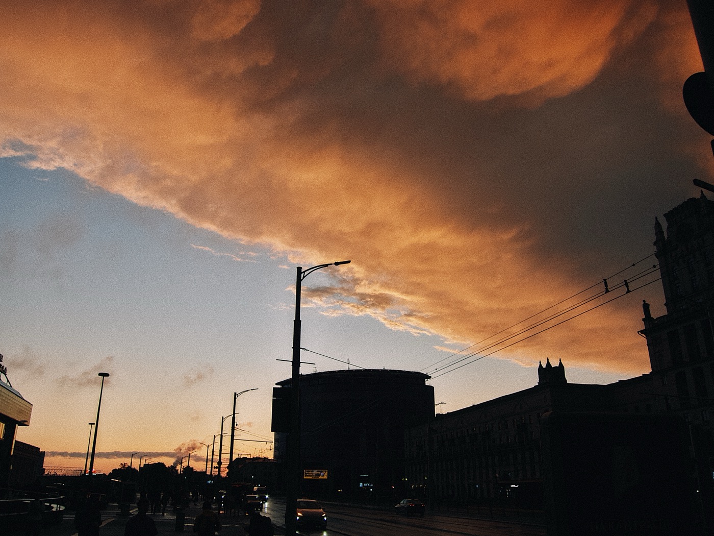 Закат с яркими облаками на фоне городских зданий и уличных фонарей.
