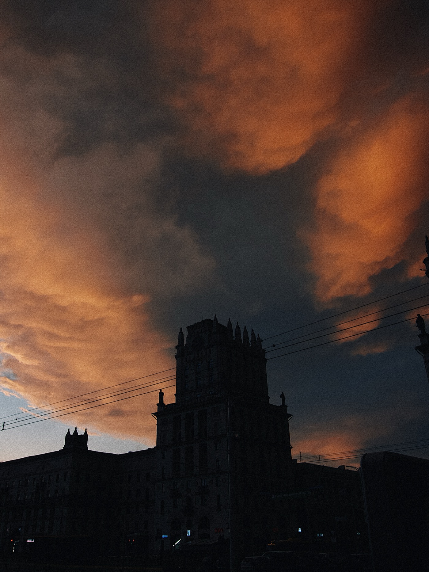 Закат с оранжевыми облаками над силуэтом здания с башнями.
