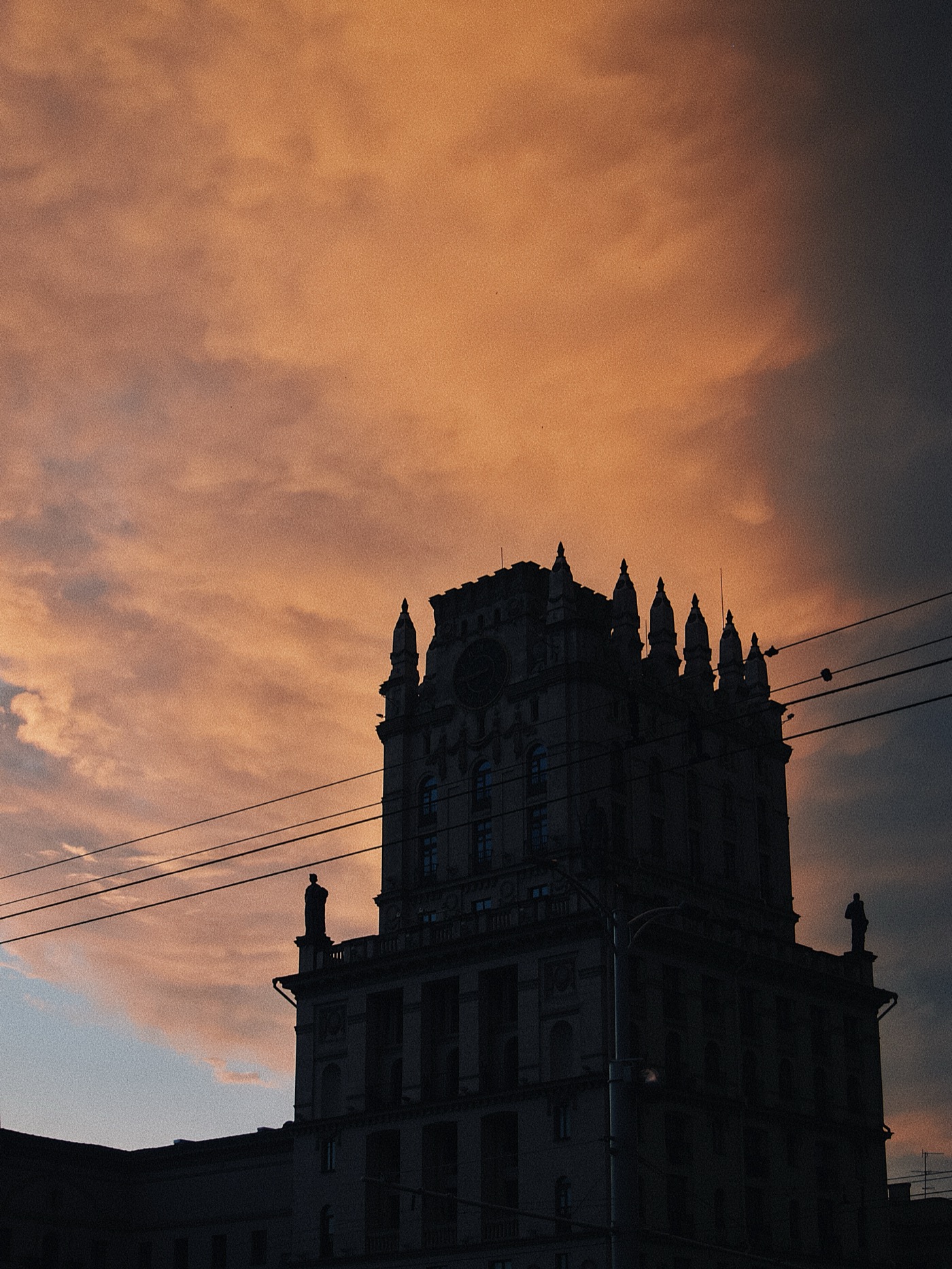 Силуэт здания на фоне яркого заката с облаками оранжевого и пурпурного цвета.