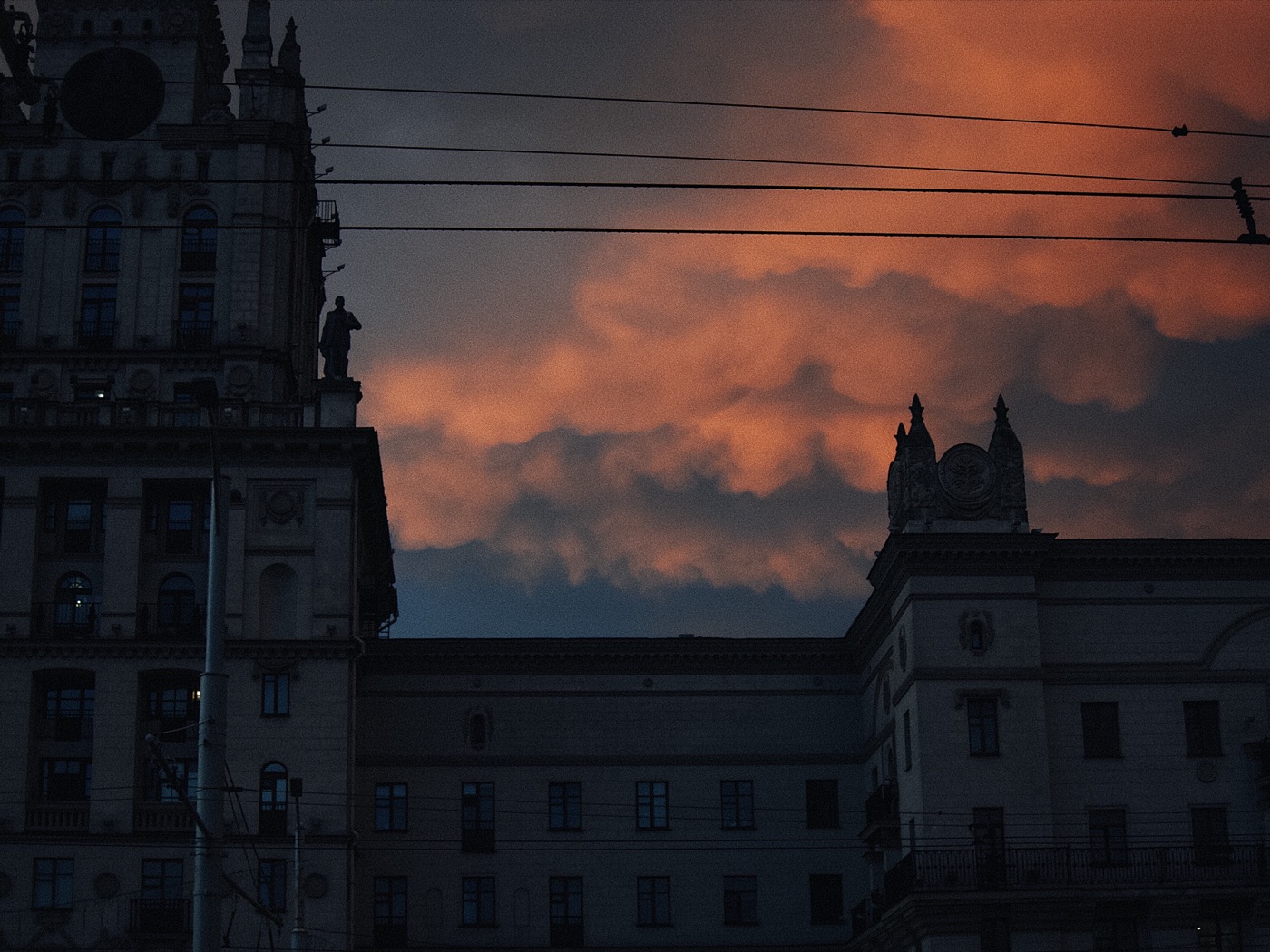 Здание на фоне яркого заката с облаками оранжевого и фиолетового цвета.