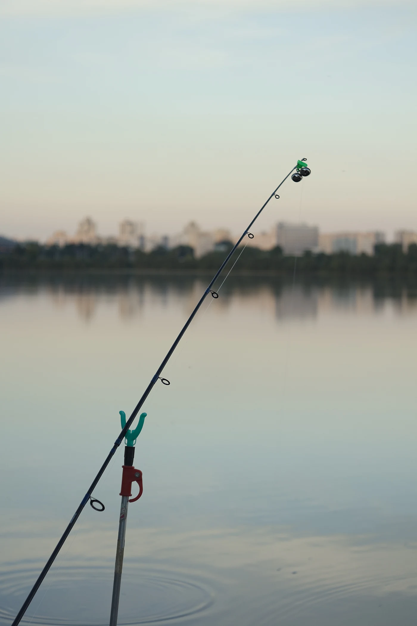 A fishing rod with a reel against a calm body of water and reflected sky.