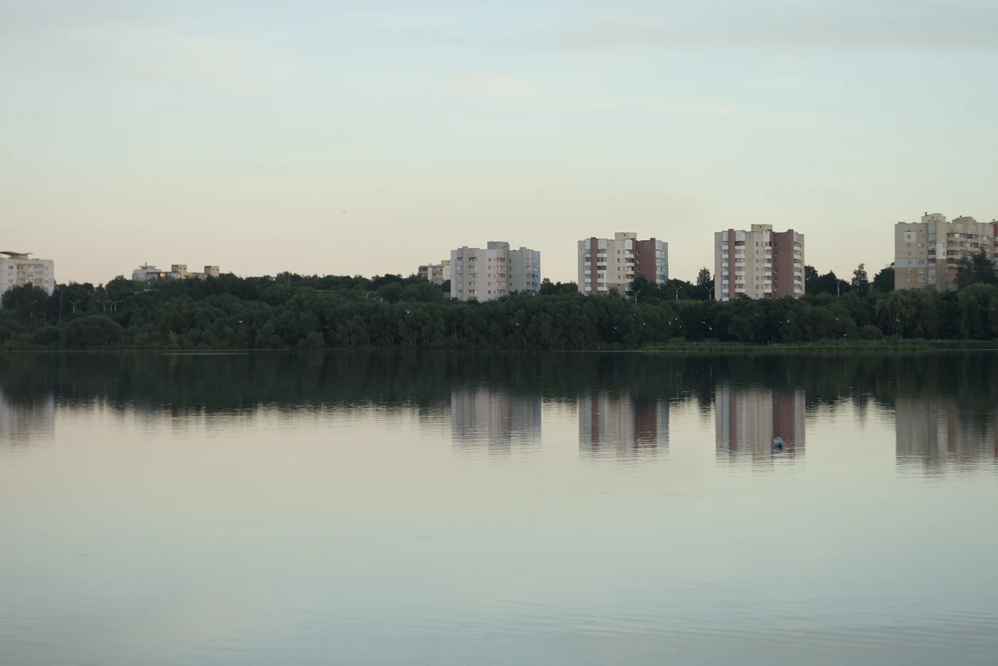The surface of the water reflects buildings on the shore; a calm atmosphere, morning or evening light.
