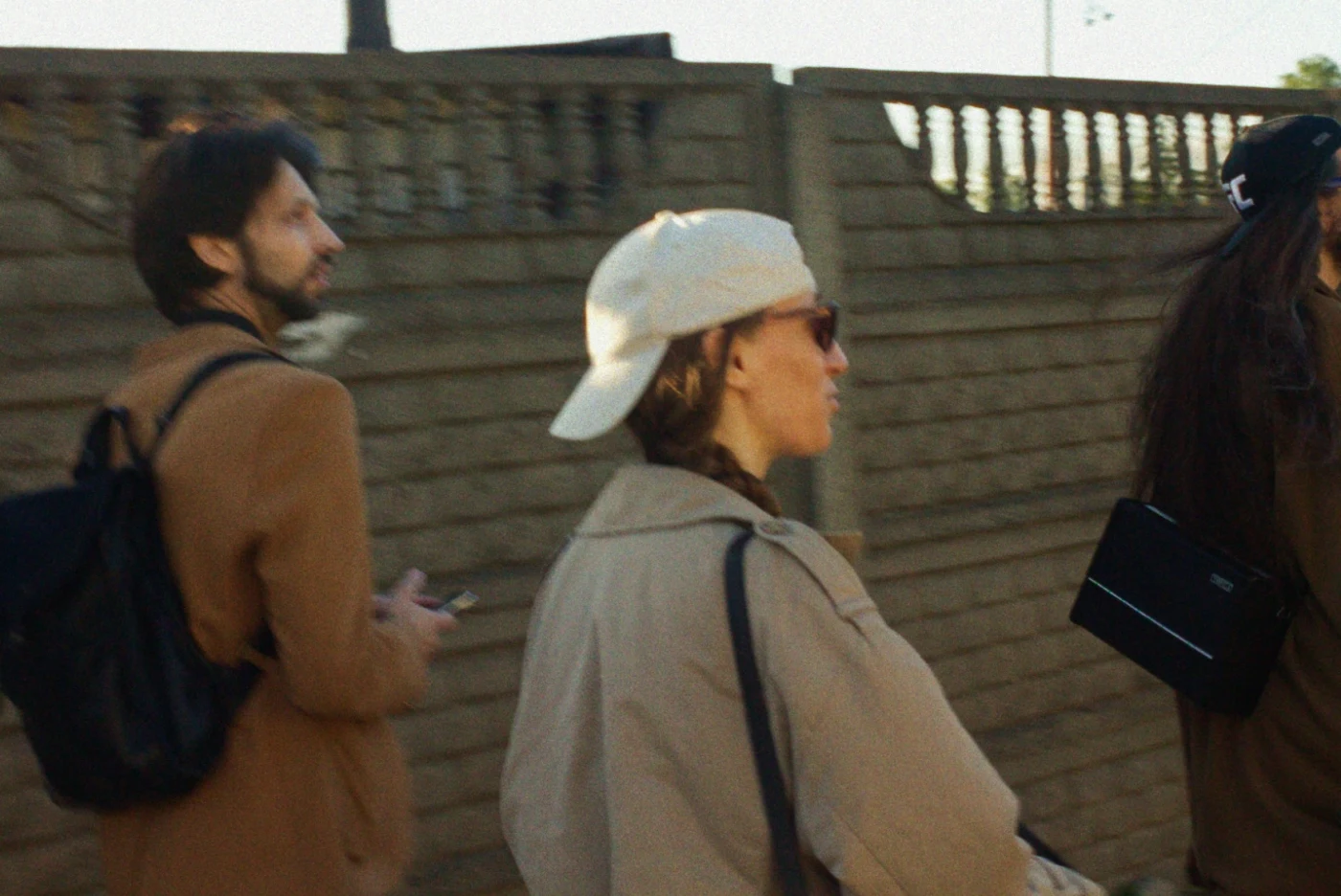 Two people on the street: a man with a backpack and a woman wearing a cap and sunglasses.