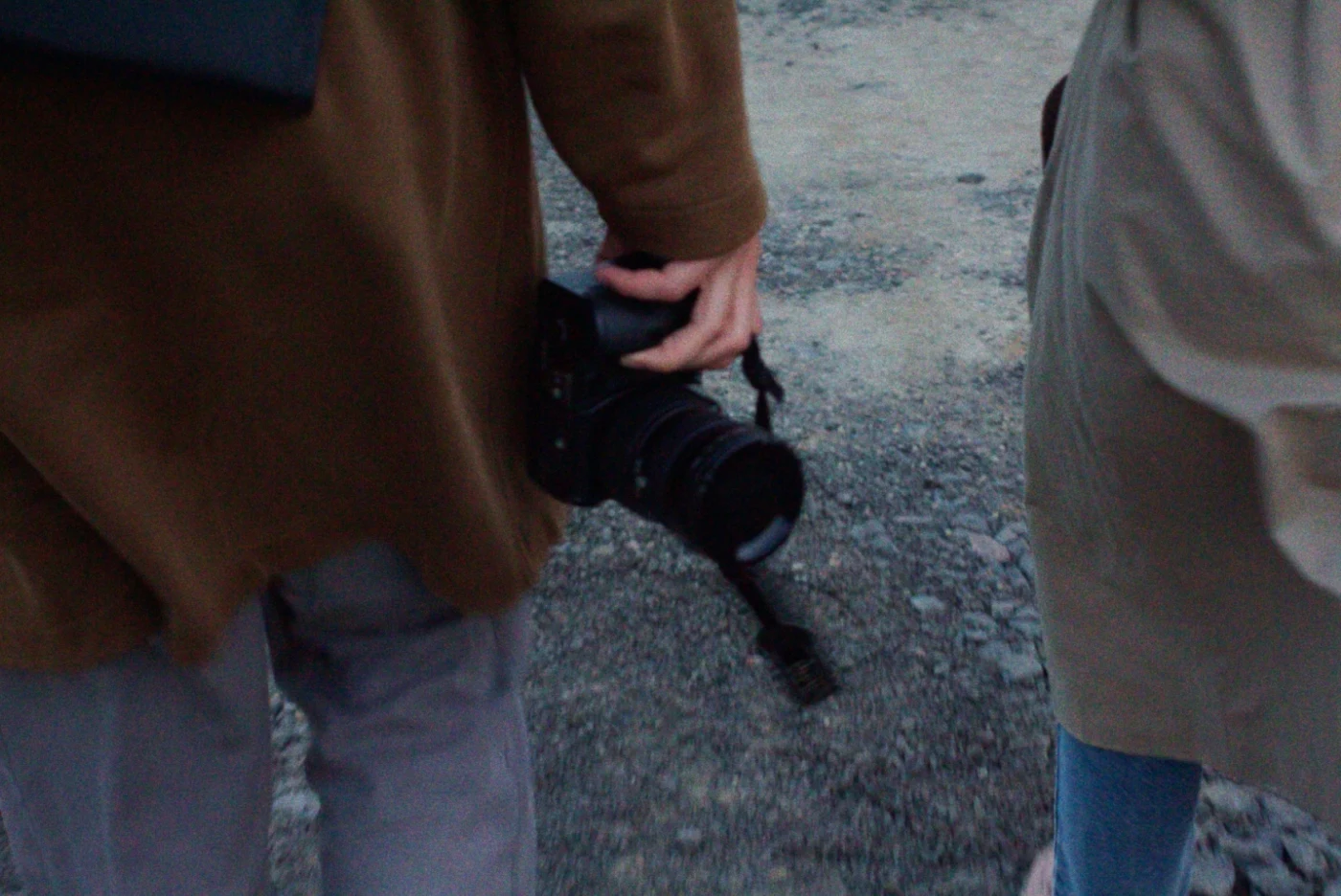 Two people walk along a road, one holding a camera in their hand.